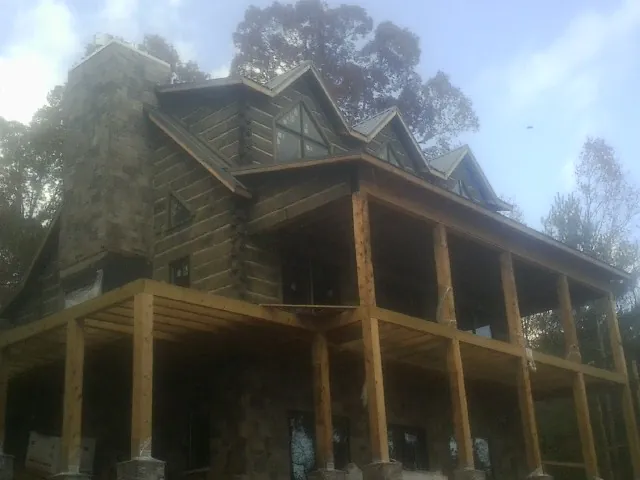 Stone chimney and dormers on a large log home with a timber porch in Danville
